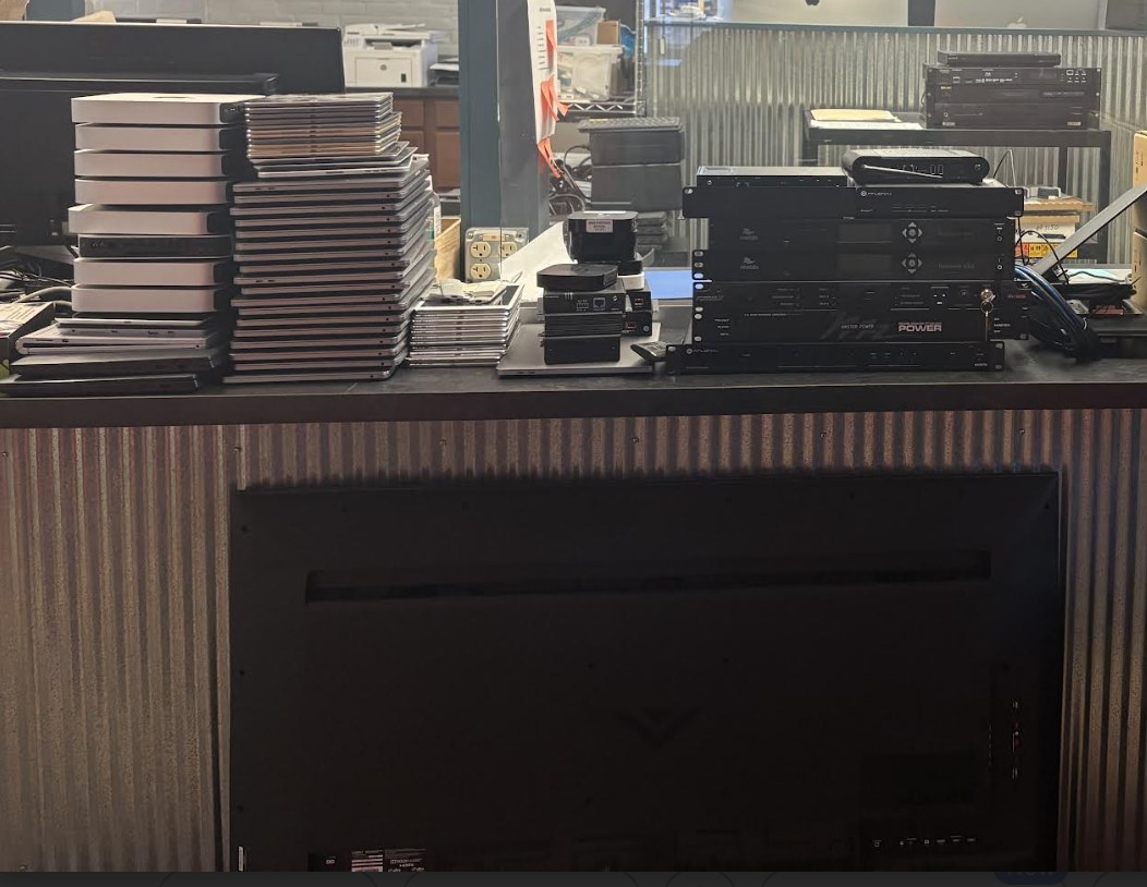 Stacked MacBooks, AV gear, monitors, and network equipment from a real refresh pickup